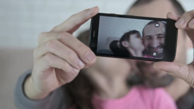 Selfie on smartphone. Father and daughter are photographed on a smartphone. A little girl kisses dad.