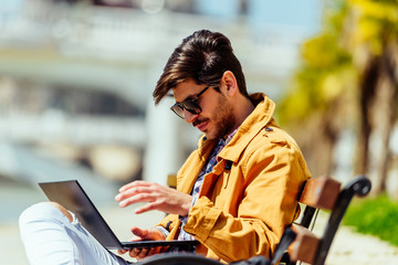 Fashionable businessman in yellow coat looking at his laptop