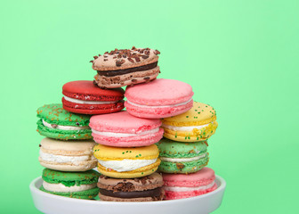Close up on Macaron cookies in various spring colors stacked on a white plate on green background. Popular French treat.