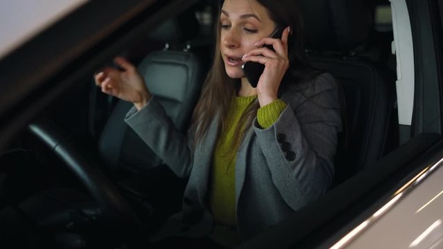 Woman is angry, upset, beating her head on the steering wheel, because her car broke down. She is trying to get help by phone.