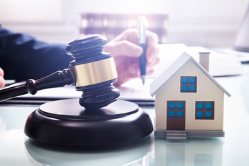 House Model With Gavel In Front Of A Businessperson