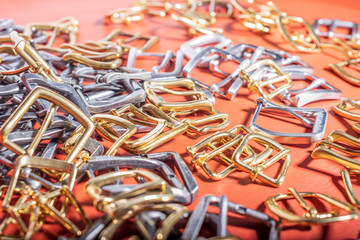 A lot of metal buckles for belts on red genuine full grain leather. Leather workshop
