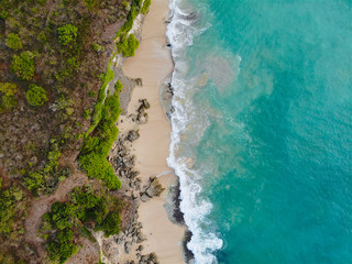 Fototapeta na wymiar Aerial view sand beach with rocks and green cliff, top view of a beautiful sandy beach with rocks and waves, aerial shot with the blue waves rolling into the shore, some rocks present