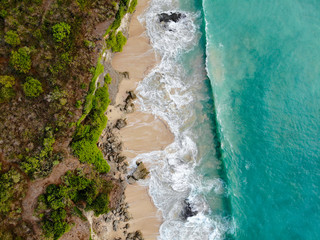 Aerial view sand beach with rocks and green cliff, top view of a beautiful sandy beach with rocks and waves, aerial shot with the blue waves rolling into the shore, some rocks present