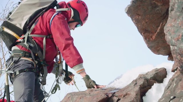 a man climber in a red suit and equipment, on his knees, climbs the mountain leaning on an ice ax.
