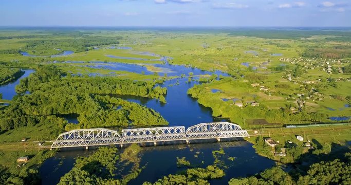 Aerial view of electric train on the railway bridge on the background of beautiful Desna river and flooded meadow at spring. Amazing water landscape of a flood-meadow. White iron bridge at countryside