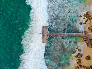 Aerial view of dock over tropical blue water and sand beach, with waves. Wooden pier in the sea. top drone view wooden jetty in blue water in Bali, Indonesia
