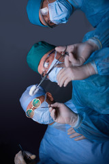 Group of surgeons at work in operating theater toned in blue. Medical team performing operation