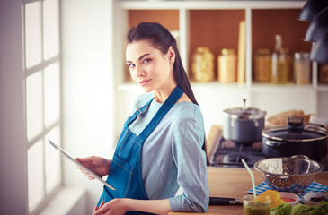 Young woman using a tablet computer to cook in her kitchen