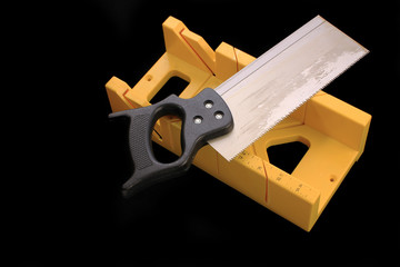 Yellow mitre box against black BG with saw laying across the mitrebox.