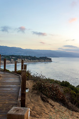 Obraz premium cliff side view of pacific ocean with boardwalk trail, plants and distant mountains
