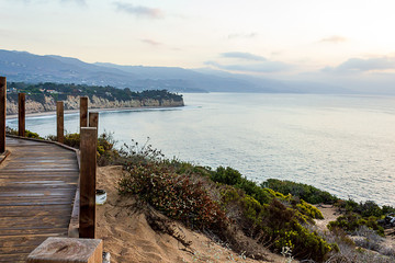 Obraz premium cliff side view of pacific ocean with boardwalk trail, plants and distant mountains