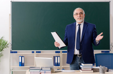 Aged male teacher in front of chalkboard 