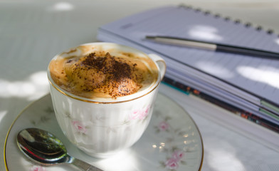 Cup of coffee with cream and notebook on an outdoor table.