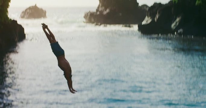 Young attractive man cliff diving into blue ocean water, tropical island cliff jumping, outdoor adventures