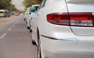 Closeup of rear, back side of white car parking in parking area beside the street in sunny day.