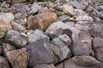 Fototapeta na wymiar Heavy rocks and boulders of different shades of greys and browns lay piled on a hill.