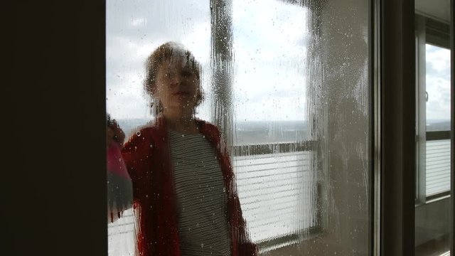 Mature woman sprays window cleaner on large window and washes it indoors - Side view