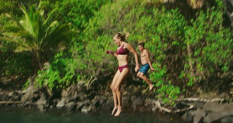 Young attractive couple cliff jumping together, young man and woman cliff jumping, summer vacation adventure