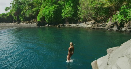Attractive young woman in bikini cliff jumping into pristine tropical water, summer outdoor adventure