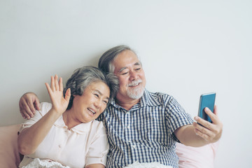 Senior couple using a smart phone computer face time call to relatives descendant relatives grandchild, smiling feel happy in bed room morning at home - lifestyle senior elderly concept