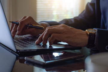 Closeup businessman in suit hand holding pen ,work on laptop computer keyboard at office.