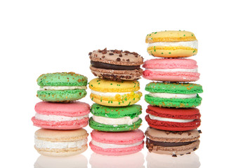Three stacks varied heights of macaron cookies, multiple colors and flavors on a reflective surface isolated on white. Traditional french treat.