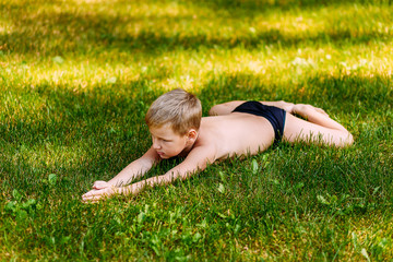 Naklejka na ściany i meble a seven-year-old flexible child in bathing trunks lies in the summer on the green grass.