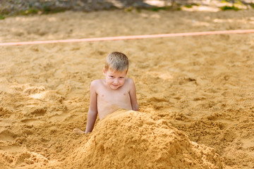 Naklejka na ściany i meble a cheerful seven-year-old boy is buried in the yellow sand on the beach.