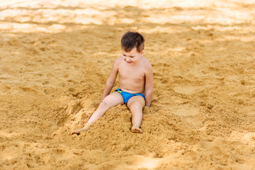 cheerful five-year-old boy sitting on the yellow sand on the beach.