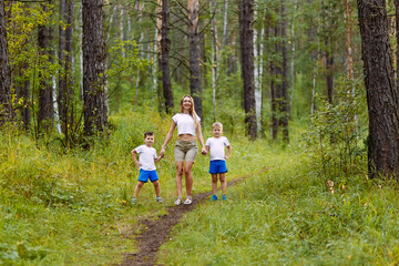 Fototapeta premium young slender mom and two preschoolers children in white t-shirts holding hands in the summer