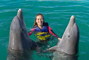Smiling woman swimming with dolphins in blue water.
