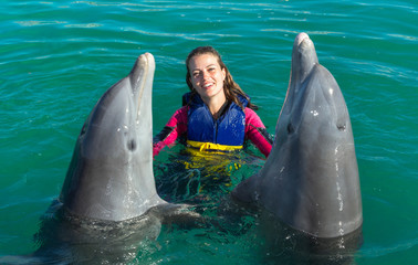 Smiling woman swimming with dolphins in blue water.