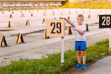 Caucasian boy in blue shorts and sneakers shows the pointer with the number "29" in the summer