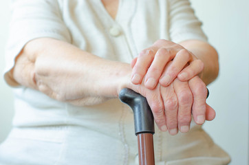 Hands of old woman holding cane, skin wrinkled