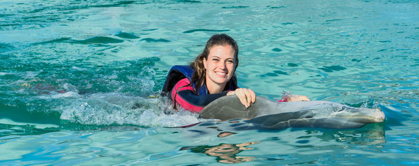 Smiling woman swimming with dolphin in blue water.