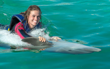 Smiling woman swimming with dolphin in blue water.