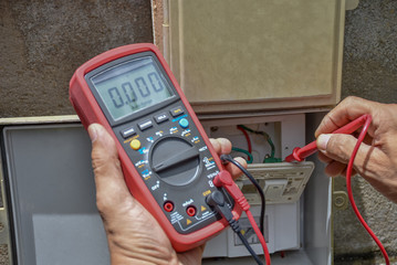 Electrical terminal box. Control panel with magnetic contactor and overload relay. Measuring voltage on main distribution board by multi meter. 