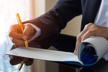 Business woman hand writing and signing check book on the wooden table at office. Paycheck or...