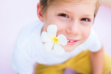 Little boy holding flower mouth pink background