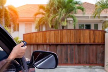 Woman in car, hand using remote control to open auto door with modern home blurred background....