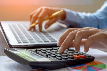 Female hand holding smartphone, using calculator to calculate about budget, work on laptop computer...