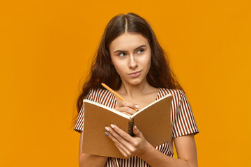 Gorgeous student girl in striped dress holding diary and pen, writing down her ideas, poems,...
