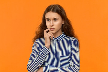 Stylish young businesswoman posing in studio with deep in thoughts pensive look, touching her chin, trying to find solution to business issue. Creative thinking, ideas and consideration concept