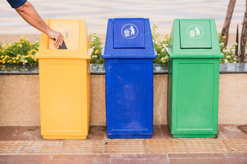 A man holding garbage into recycle bin.Row of different waste bin at the public park.