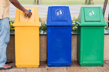 A man holding plastic bottle water into recycle bin.Row of different waste bin at the public park