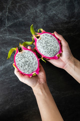 Dragon fruit in man hands with black marble background, top view.