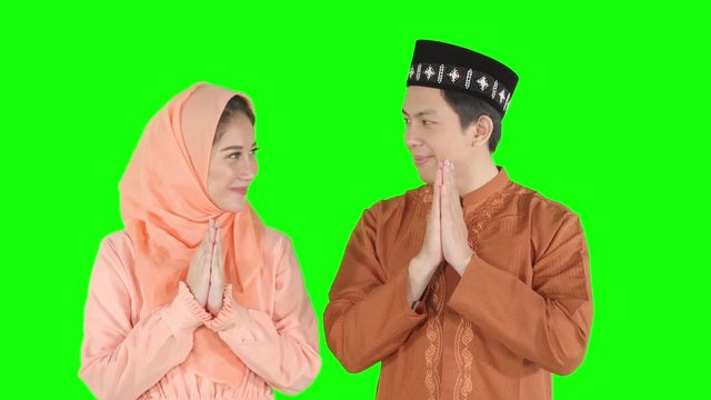 Attractive muslim couple showing a greeting hands gesture and smiling to each other in the studio