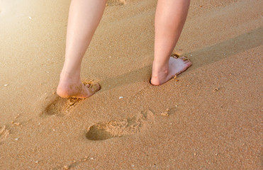Woman walking on the beach leaving footprints on fine soft sand.