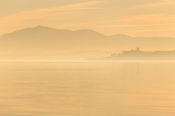 Beautiful view of Trasimeno lake at sunset with birds on water and Castiglione del Lago town
